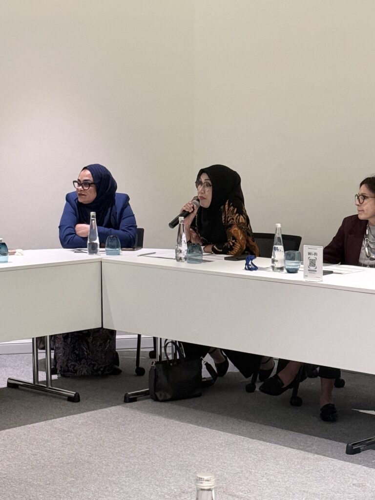 A woman speaks into a microphone at the classroom table.