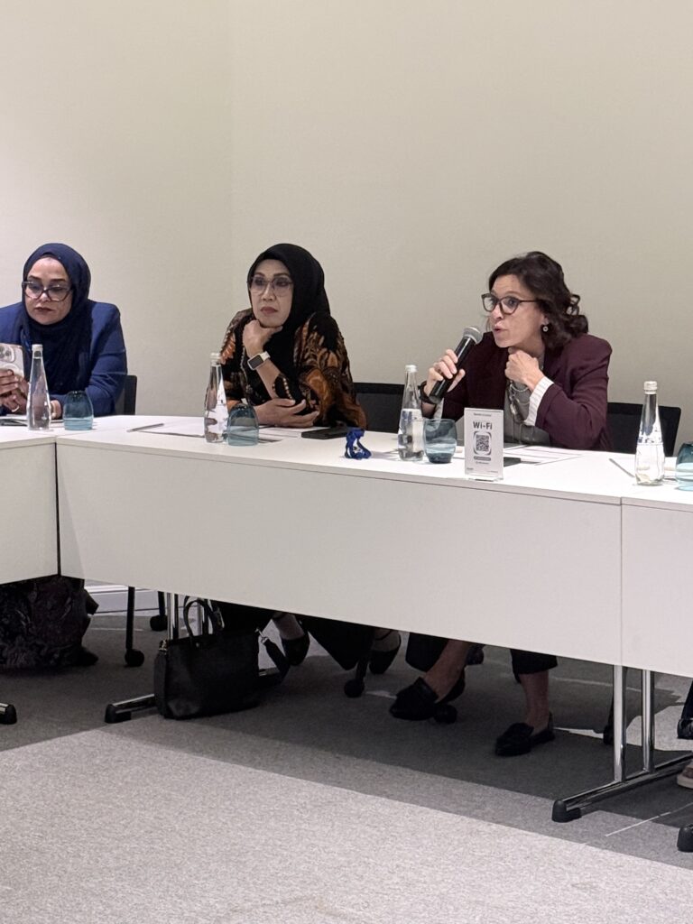 A second woman speaks into a microphone with colleagues seated beside her.
