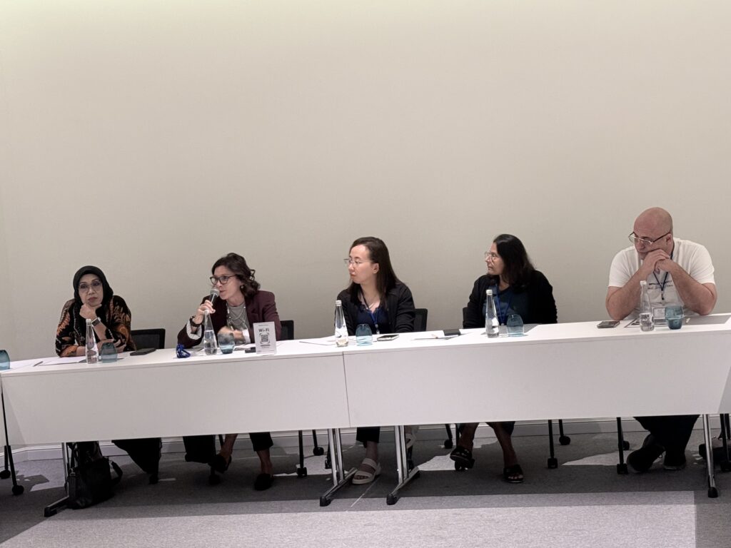 Several participants sit at a table as one woman speaks into a microphone.