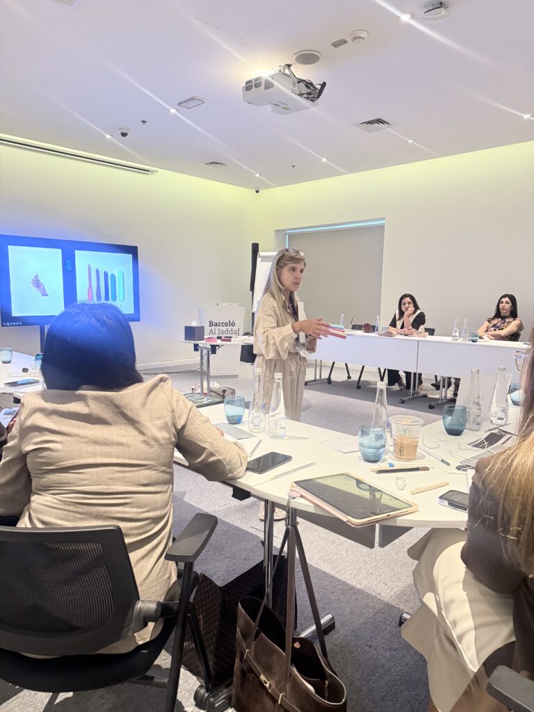 A woman speaks to participants in front of projected teaching material.