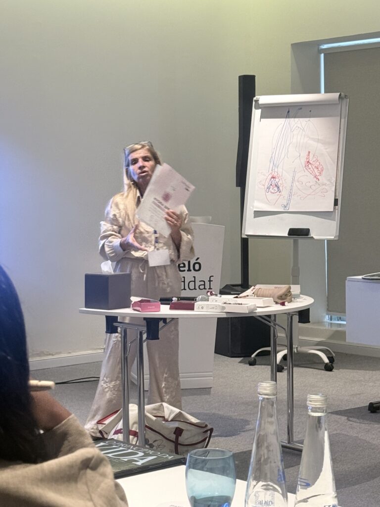 A presenter holds a sheet beside an illustrated flip chart.