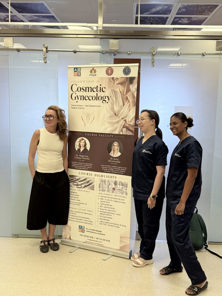 Three women pose beside the Fellowship in Cosmetic Gynecology course banner.