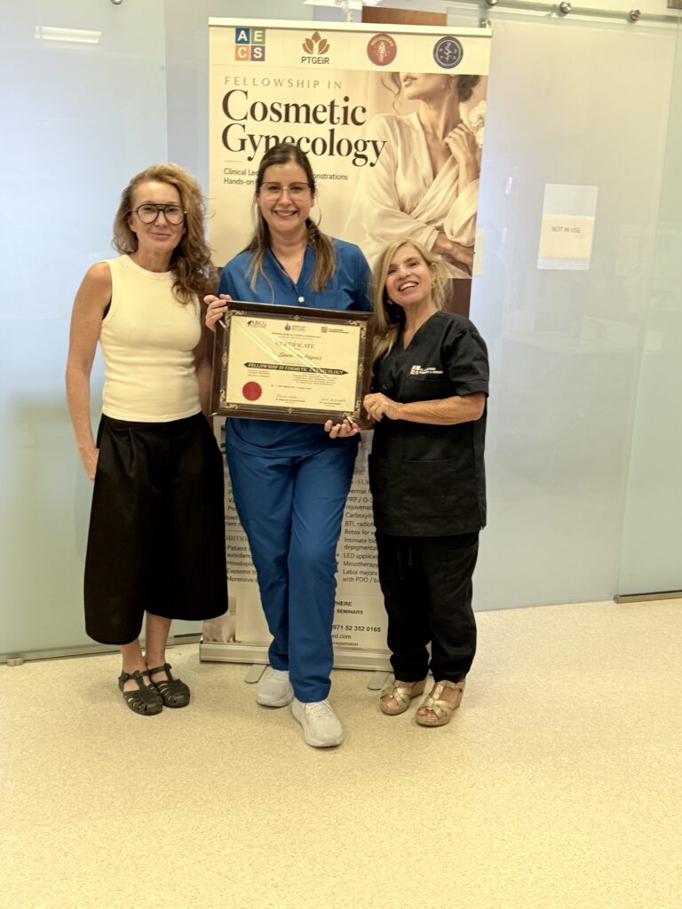 A woman in blue scrubs displays her course certificate between two women.