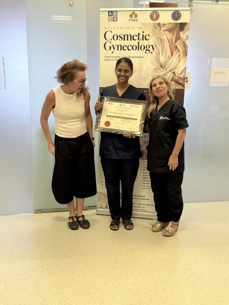 A woman in dark scrubs displays her certificate beside two women.