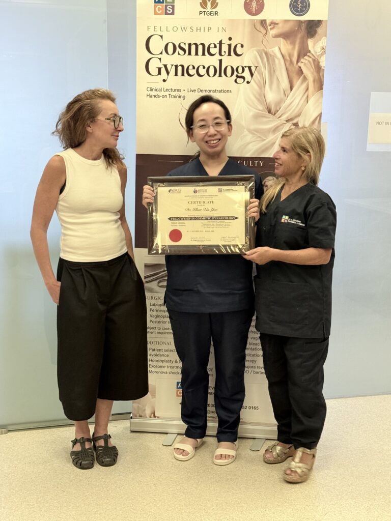 A woman in navy scrubs displays her certificate beside two women.