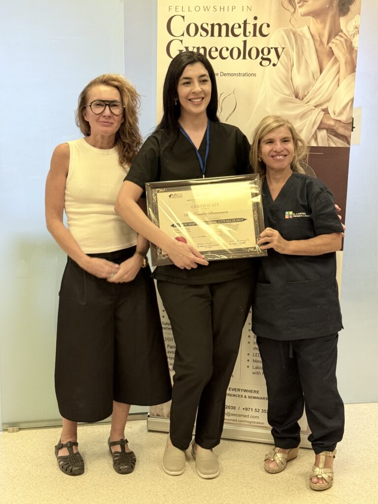 A woman in black scrubs displays her certificate beside two women.