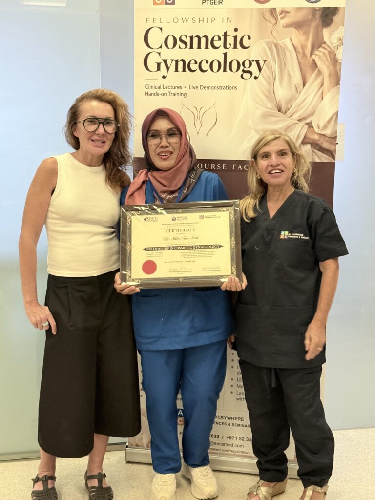 A woman in a rose-colored headscarf and blue scrubs displays her certificate.